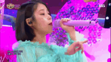 a woman singing into a purple microphone with sbs written on the bottom right