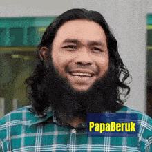 a man with long hair and a beard is wearing a green plaid shirt and has a papaberuk sticker on his shirt