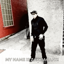 a man wearing sunglasses and a hat is dancing in front of a red brick building .