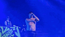 a man without a shirt is singing into a microphone in front of a sign that says ' naruto ' on it