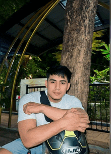 a man leaning against a tree with a helmet that says hjc