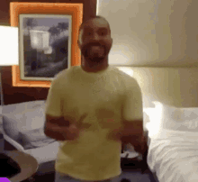 a man in a yellow shirt is giving a thumbs up in a hotel room