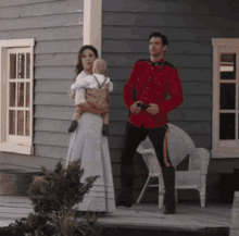 a man in a red uniform holds a baby while a woman in a white dress holds a baby