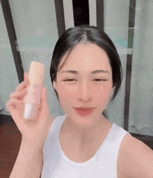 a woman is wearing a white tank top and holding a bottle of lotion .