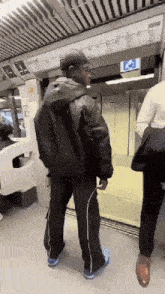 a man in a black jacket and hat is standing in an elevator