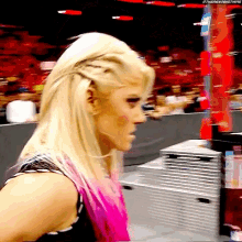 a woman with blonde hair and pink highlights stands in front of a stack of boxes