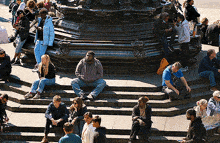 a group of people sit on the steps of a statue