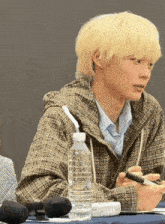 a man in a plaid jacket sits at a table with a bottle of water in front of him