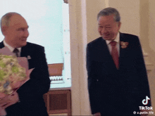 a man in a suit and tie is holding a bouquet of flowers next to another man in a suit and tie