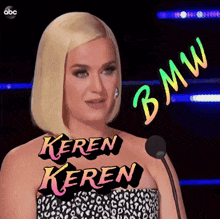 a woman in a leopard print dress stands in front of a microphone with the words keren keren on her chest