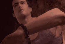 a man wearing a tank top and a necklace is looking down at something .