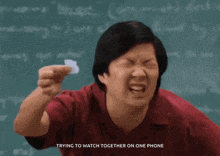 a man in a red shirt is holding a piece of paper in front of a chalkboard .