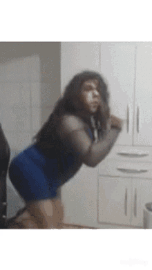 a woman in a blue dress is squatting down in front of a white cabinet .