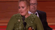 a woman in a green dress is crying while standing in front of a microphone at awards .