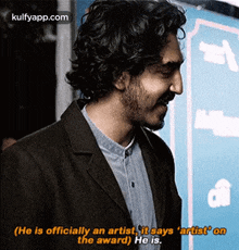 a man with curly hair and a beard is wearing a black jacket and a blue shirt .