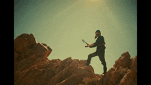 a man in a mask is holding a sword on top of a rocky cliff