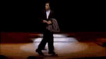 a man in a suit is walking on a stage in front of a crowd of people .