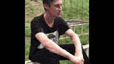 a man in a black t-shirt is sitting on a bench .