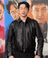a man wearing a black leather jacket is standing in front of a poster of a man wearing glasses