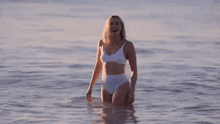a woman in a white bikini stands in the water with her arms outstretched
