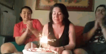 a woman is blowing out candles on a birthday cake while sitting on a couch with two other people .