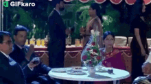 a group of people are sitting at a table with plates and flowers .