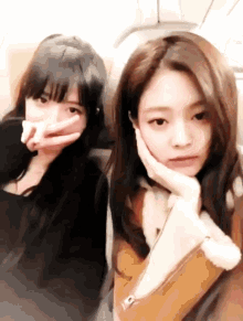 two girls are sitting next to each other and one is covering her face with her hand