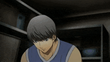 a man in a blue tank top is looking down in a dark room