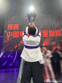 a man is holding a trophy in front of a banner with chinese characters on it