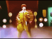 a mcdonald 's clown is dancing on a stage in front of a bunch of lights