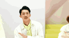 a man wearing a white jacket and a yellow shirt is clapping his hands .