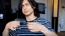 a young man in a striped shirt is sitting in a chair and holding something in his hands .
