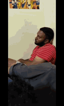 a man in a red and white striped shirt is sitting in front of a wall with a picture of dragon ball z on it