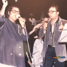 a man singing into a microphone next to another man holding a guitar