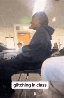 a man is sitting in a chair in a classroom with other people .