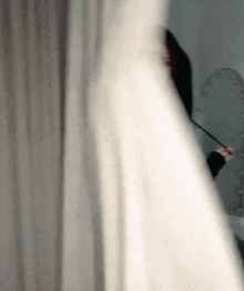 a woman in a white dress is holding a wand behind a white curtain .