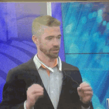 a man in a suit stands in front of a large screen