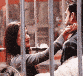 a woman is touching a man 's face behind bars with a clock in the background