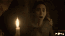 a woman is crying in front of a lit candle with imgplay written on the bottom right