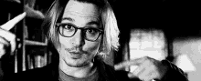 a black and white photo of a man wearing glasses and pointing at something .