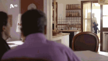 a man in a purple shirt sits at a table in front of a sign that says hd