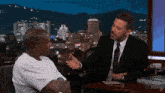 a man in a white shirt sits at a table with a man in a suit and tie