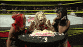 three women are standing around a table with a cake on it and one of them has cake on her face