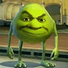 a green monster from the movie monsters inc is standing on a sidewalk and looking at the camera .