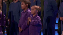 a boy and a girl are standing next to each other in front of a choir wearing purple jumpsuits .