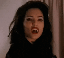 a woman with long black hair and vampire teeth is screaming .