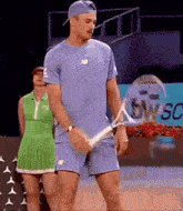 a man is holding a tennis racquet while a woman stands behind him in a green dress
