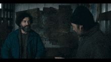 a man with a beard and a beanie is talking to another man