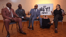 a group of men are sitting in front of a sign that says hey