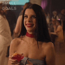 a woman is smiling while holding a glass of red liquid with the words small achievable goals behind her
